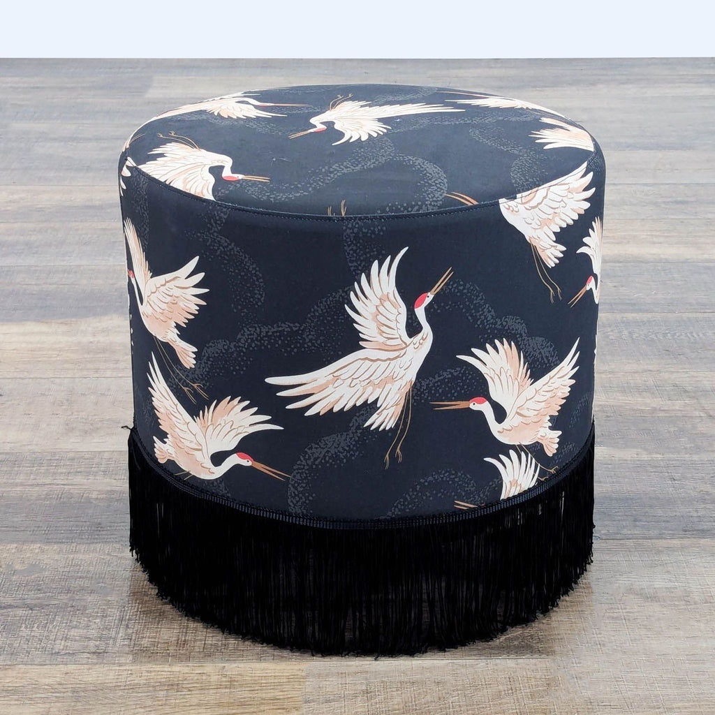 1. Round ottoman from Skyline Furniture with a navy crane pattern and black fringe at the base, on wooden floor.