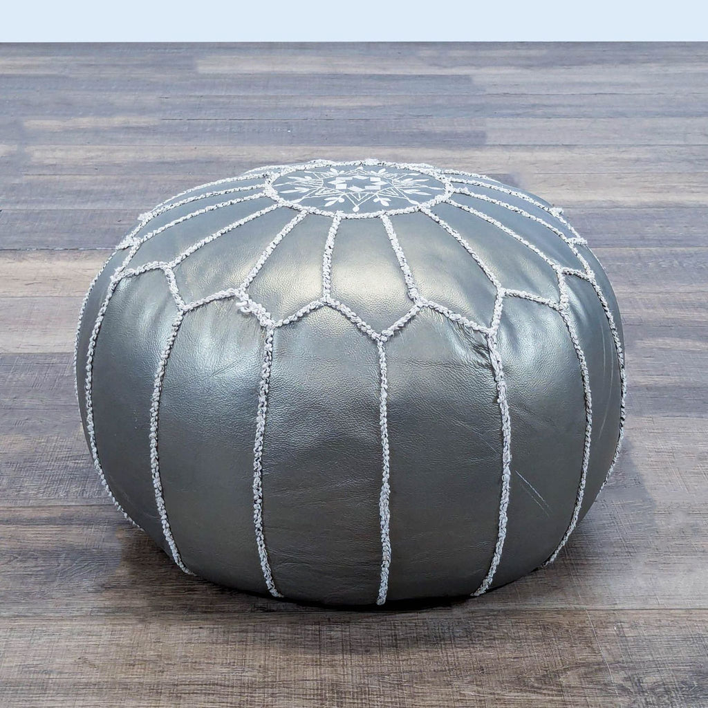 1. Silver round ottoman with white decorative stitching by Reperch, placed on a wooden floor.
