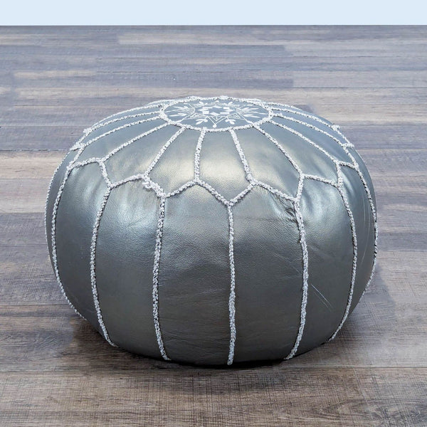 1. Silver round ottoman with white decorative stitching by Reperch, placed on a wooden floor.