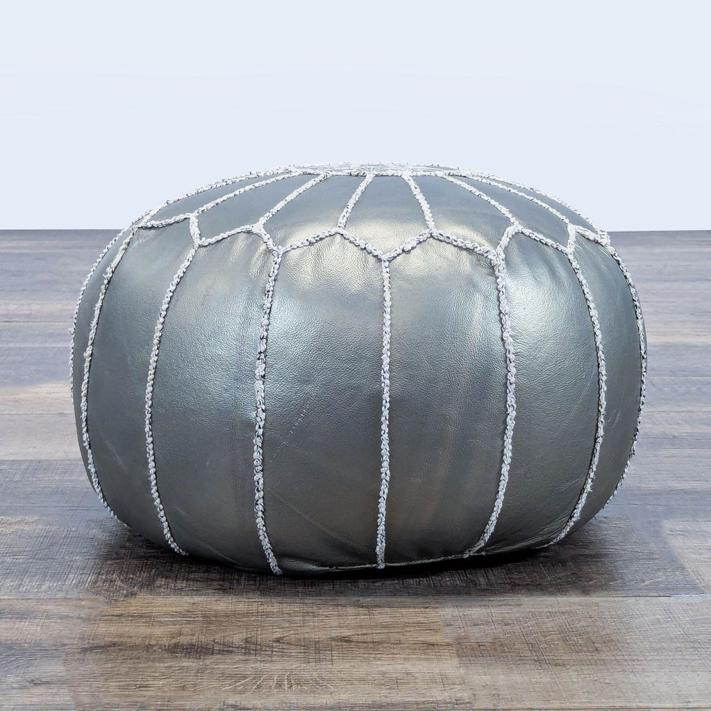 3. Side view of a metallic silver Reperch ottoman with vertical and arched white stitching detail.