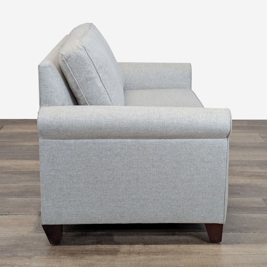 2. Side profile of a Pottery Barn loveseat showing the rolled arm and cushion design on wooden floors.