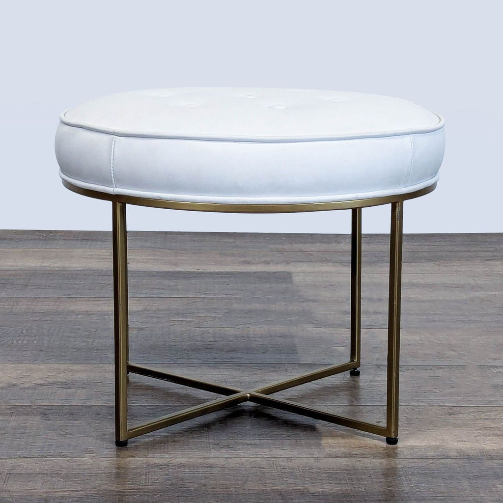 1. Round white Reperch ottoman with button-tufted top and gold metal X-base on wood flooring.