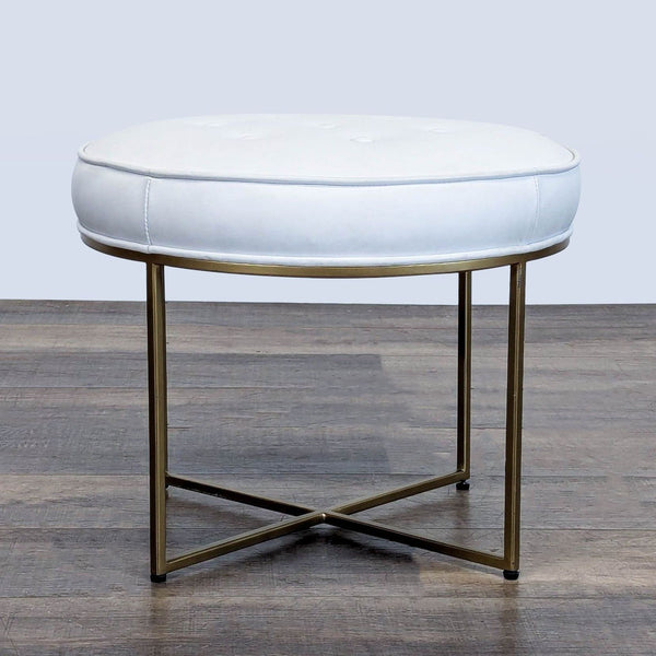 1. Round white Reperch ottoman with button-tufted top and gold metal X-base on wood flooring.