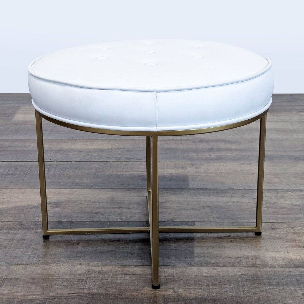 3. Modern Reperch ottoman featuring a round white cushion and slim gold metal legs, seen from the front.