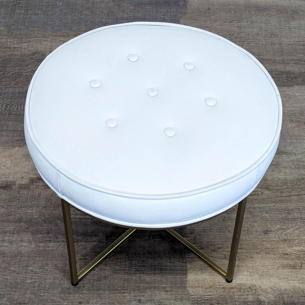 2. Top view of Reperch round ottoman, white cushioned seat with button accents and gold crisscross base.