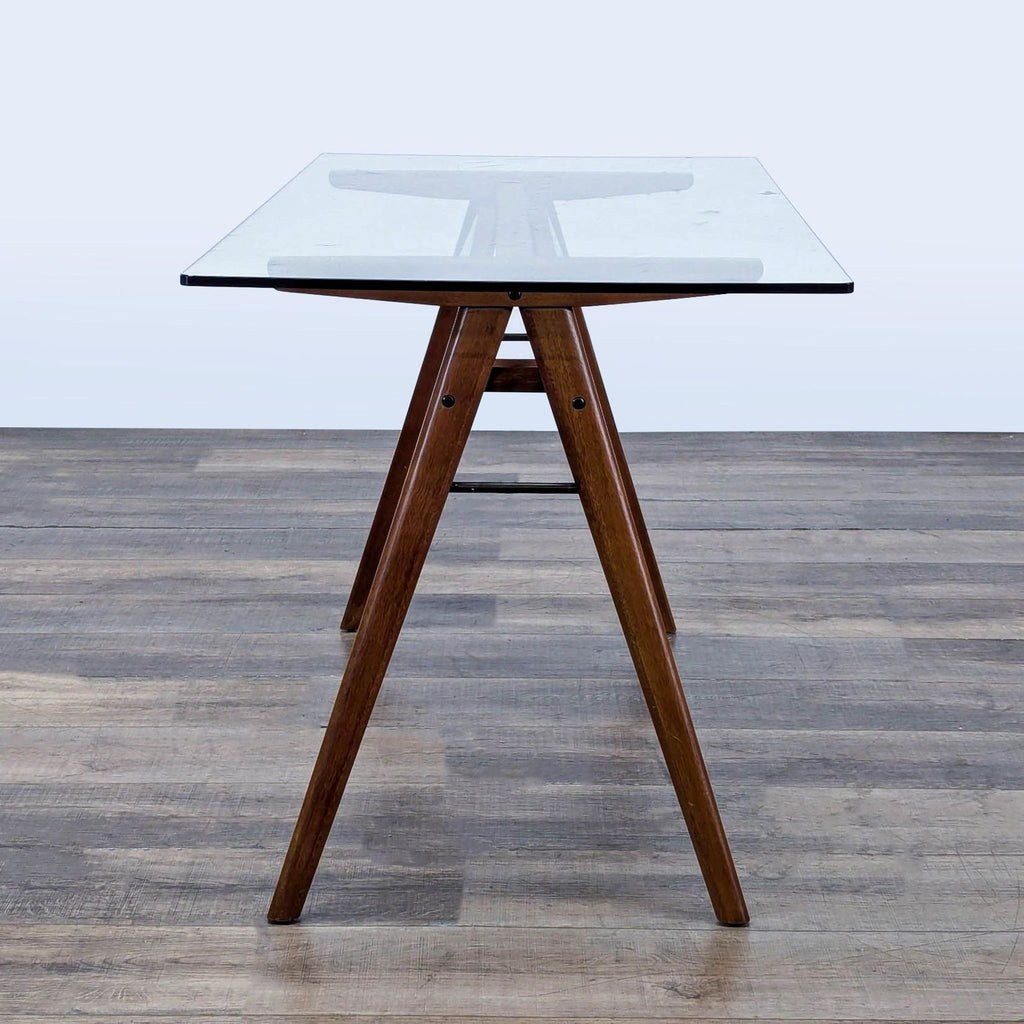2. Side view of a West Elm desk featuring a glass surface and A-frame solid wood base, placed on wood flooring.