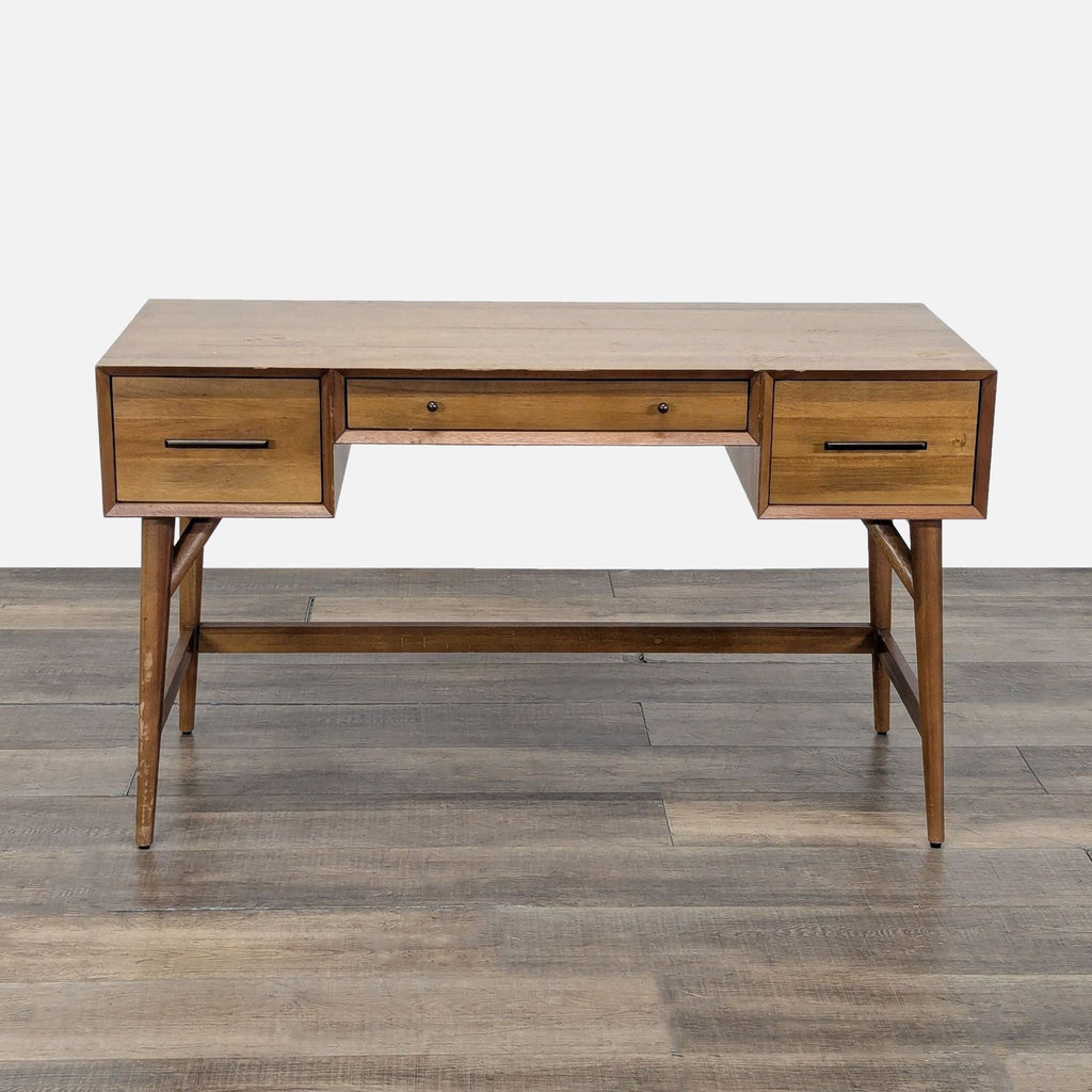 1. Mid-century style West Elm desk in acorn finish, with three drawers and splayed legs on a wood floor.