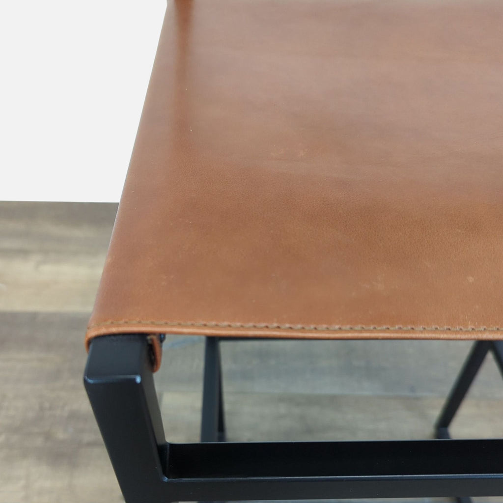 2. Close-up of Reperch bar stool showing smooth brown leather seat and sturdy black metal corners.