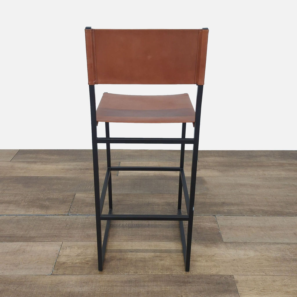 3. Rear view of Reperch bar stool with brown leather backrest and black metal frame on wooden floor.