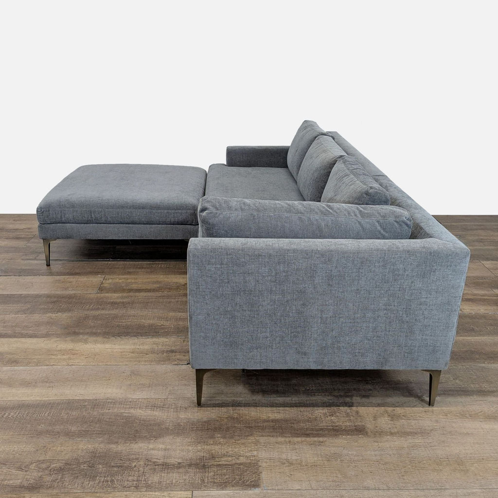 Side view of a Reperch sectional featuring slim arms, a slender seat deck, and tall cast metal legs in gray fabric.  