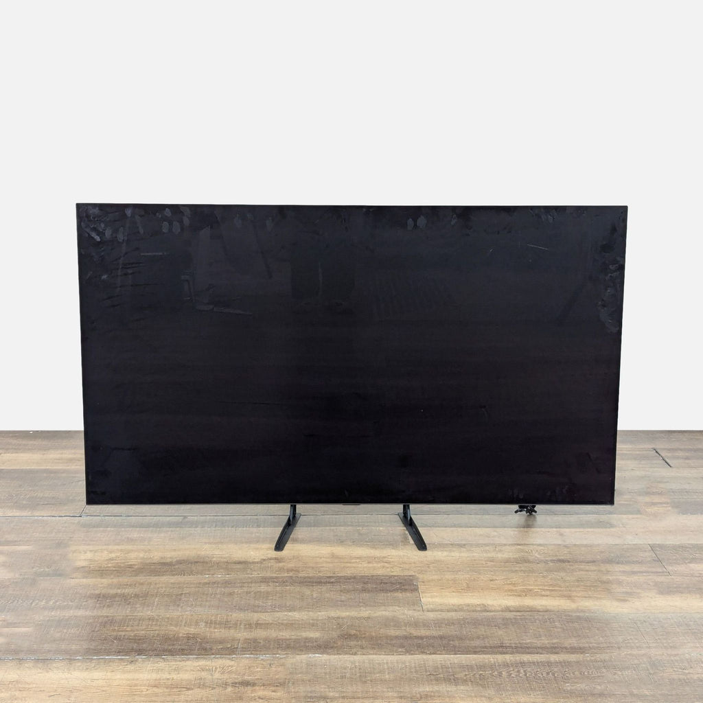 1. Front view of a 65-inch LG OLED TV with a large black screen and slim dual legs on wooden flooring.  