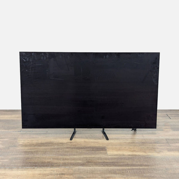 1. Front view of a 65-inch LG OLED TV with a large black screen and slim dual legs on wooden flooring.  