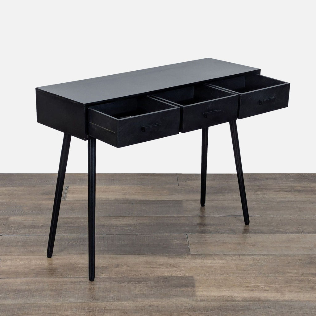 2. Angled view of Reperch black console table, featuring three open drawers and slender legs.