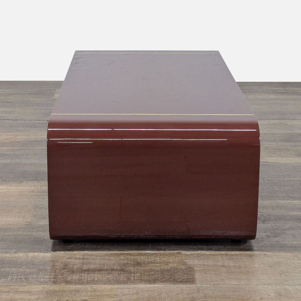 Side view of Arteriors coffee table showcasing glossy paprika finish, brass inlay, and curved angular base design.