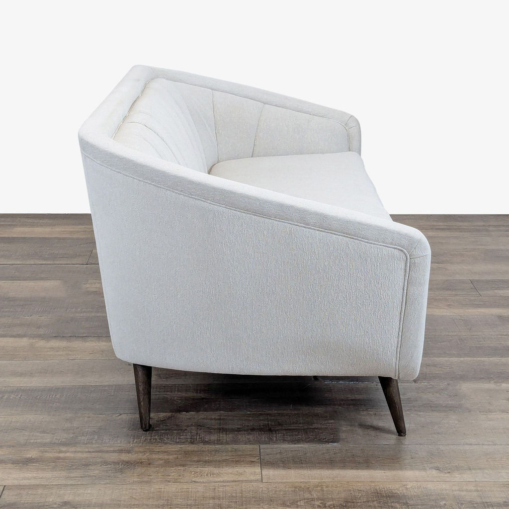 2. Side view of a Four Hands 3-seat sofa showing curved lines, channel tufting, and slender wooden legs.