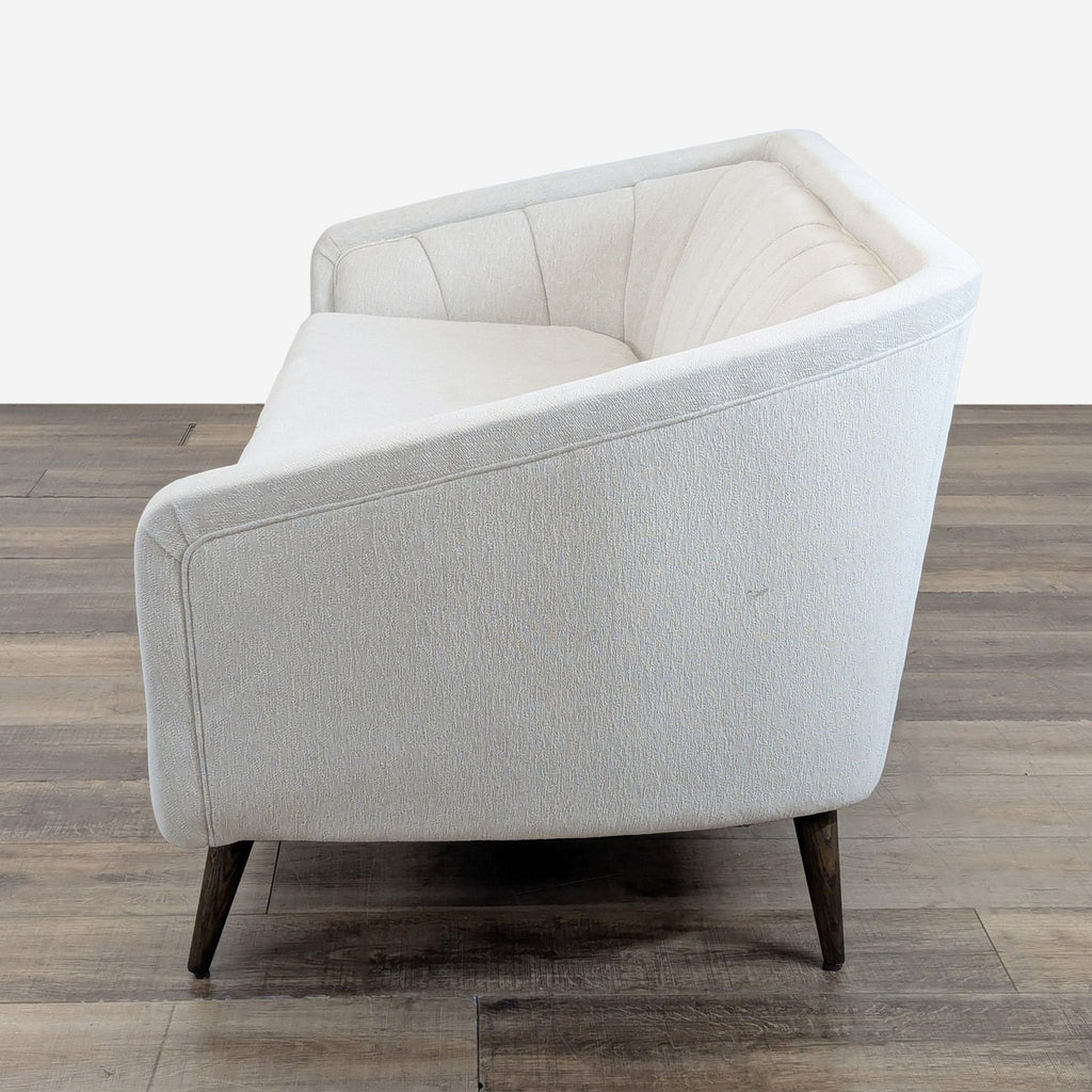 3. Angled rear view of a Four Hands 3-seat sofa, featuring curved lines and channel tufting on light fabric.