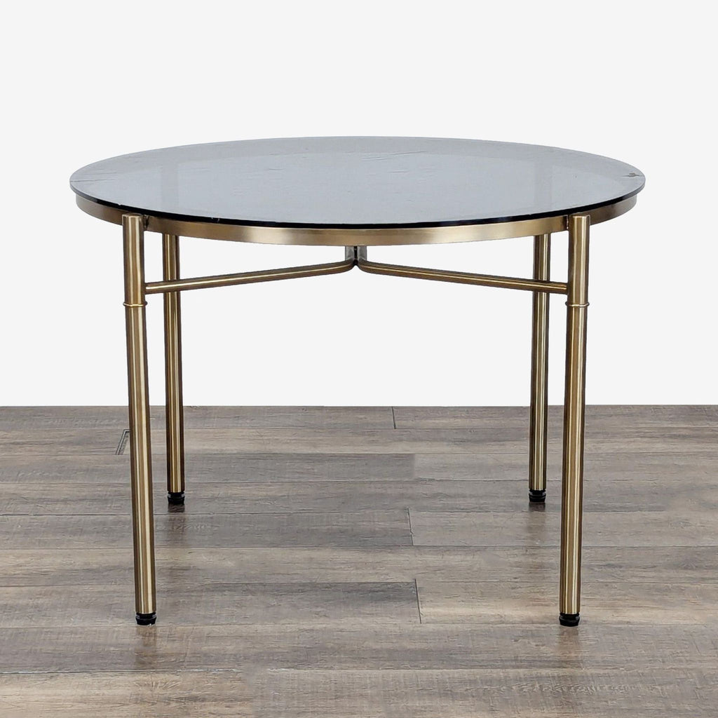 Round table with metal base by Reperch, featuring a glass top and brass-colored legs on wood floor.  