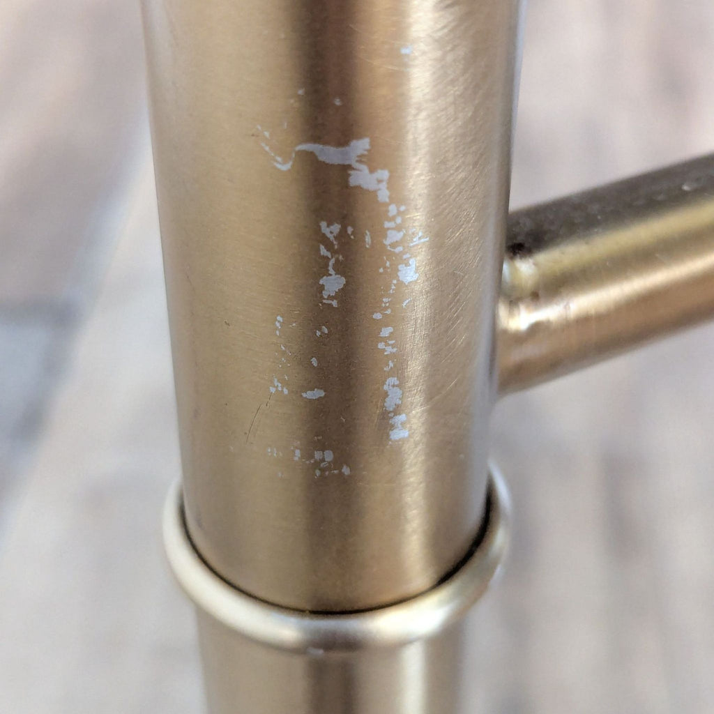Detail of Reperch dining table’s metal leg showing paint wear and scratches on the gold surface.