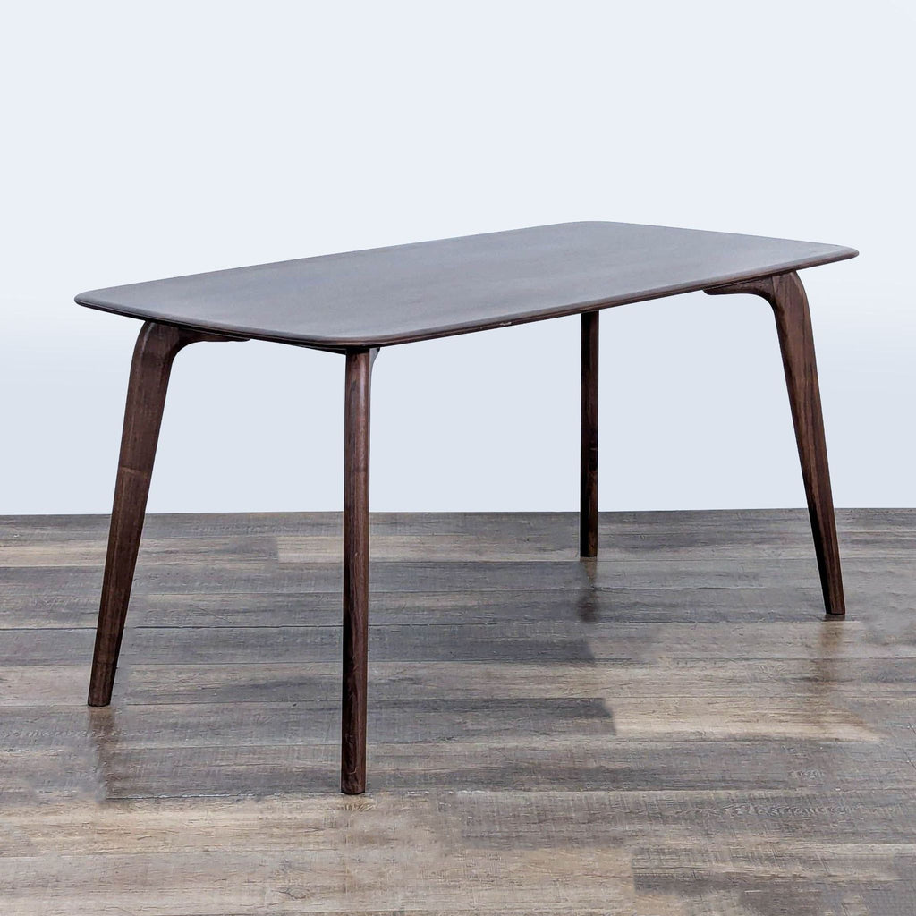2. Angled view of a Castlery dining table with a smooth dark wood top and gently curved legs.  