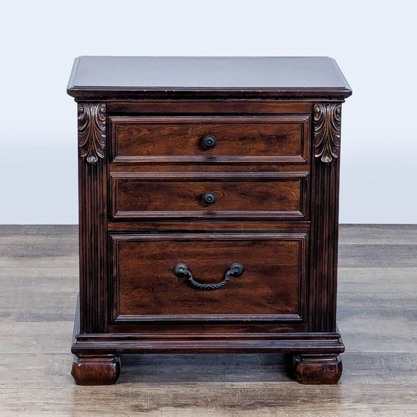 Classic wood nightstand by Ashley Furniture with three drawers, ornate brass knobs, and carved accents.