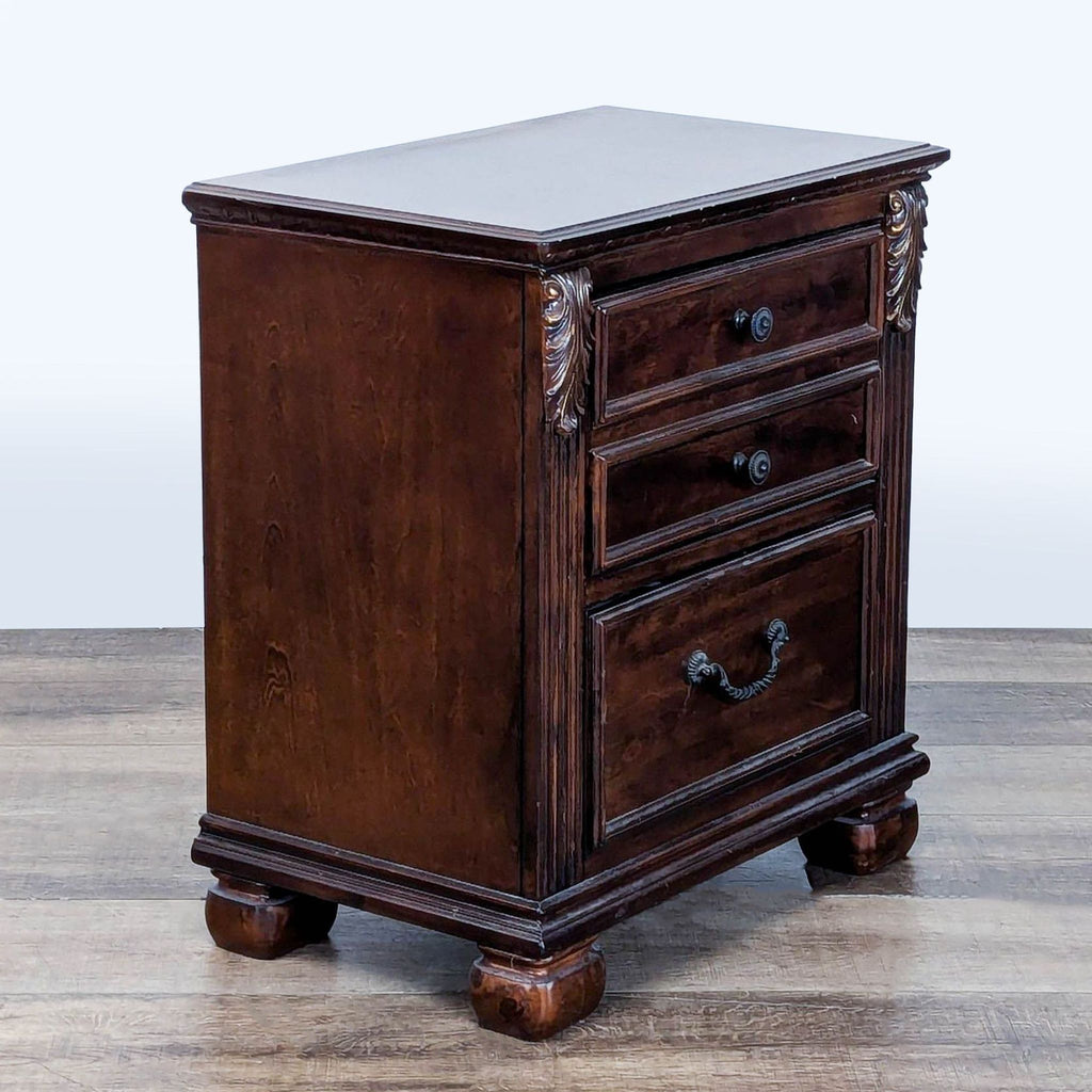 Three-drawer dark wood end table by Ashley Furniture, featuring antique brass hardware and decorative corbels.