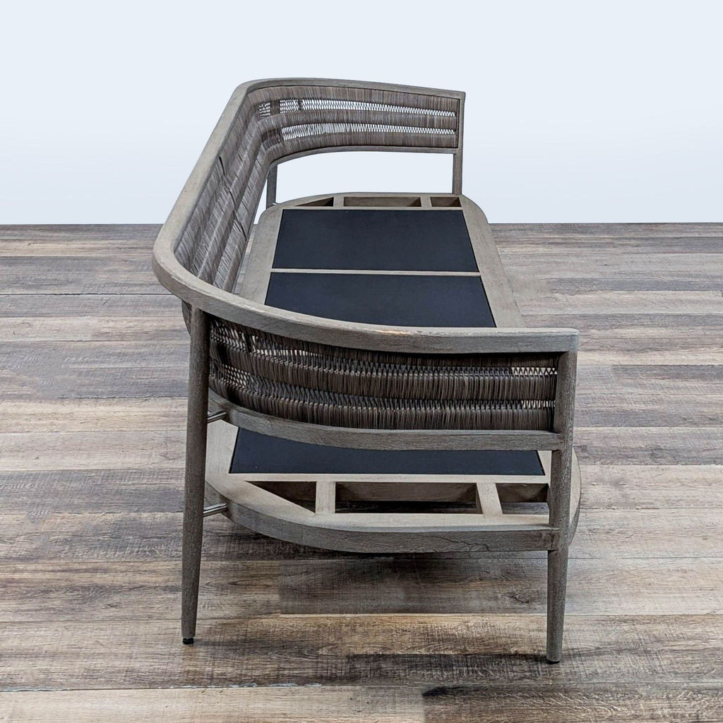 2. Side view of a Restoration Hardware chair, showing curved wicker backrest and sturdy teak frame without cushions.  