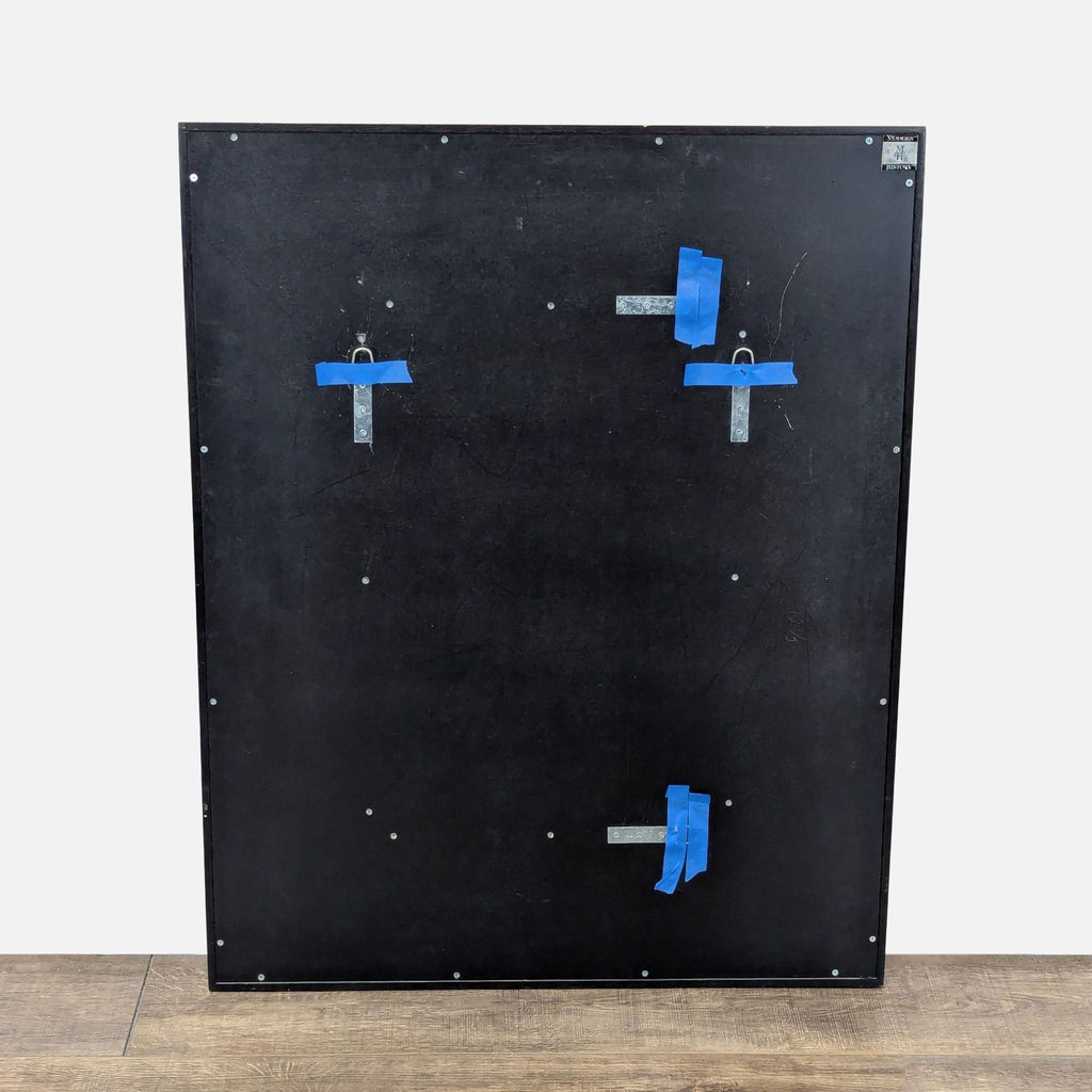 2. Rear view of the Modern History mirror showing a solid black back panel with metal brackets and blue tape.