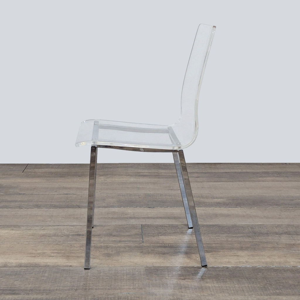 2. Side profile of a CB2 chair featuring a transparent acrylic seat and slim, metallic nickel legs.