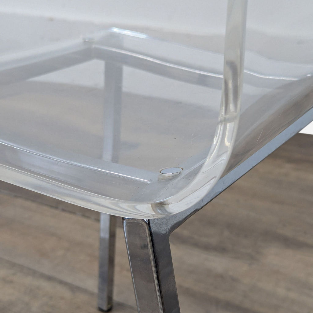 3. Close-up of the CB2 chair’s clear acrylic seat and shiny nickel leg, highlighting its modern design.
