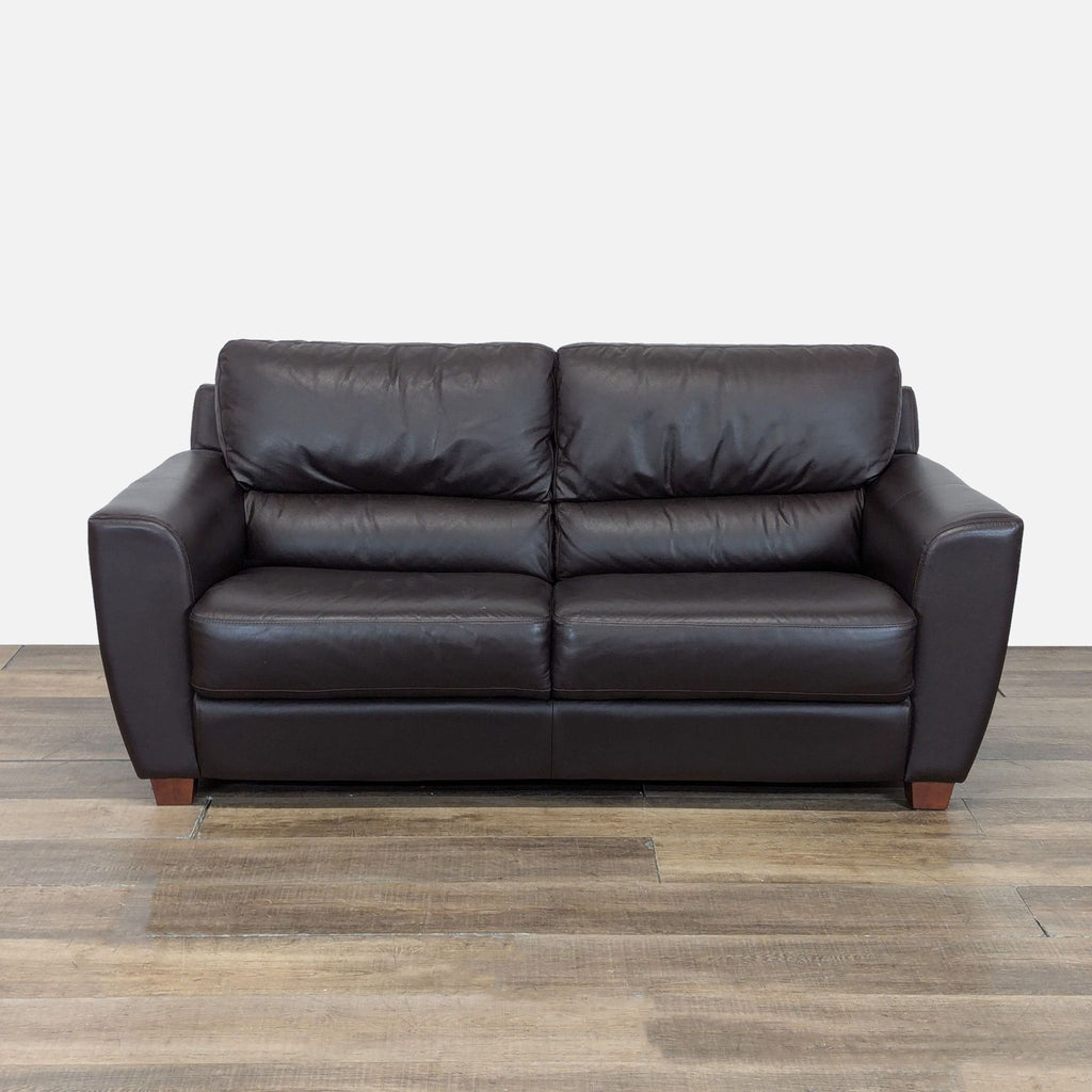 Front view of an Ikea 3-seat sofa with leather upholstery and tapered wood block feet on a wooden floor.