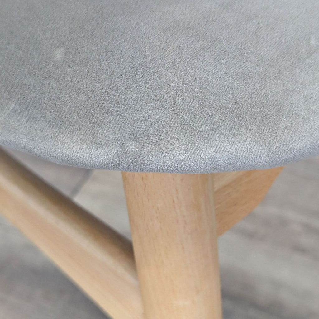 Close-up of the upholstered seat on a Reperch dining chair, highlighting the soft grey fabric and ash wood frame.  