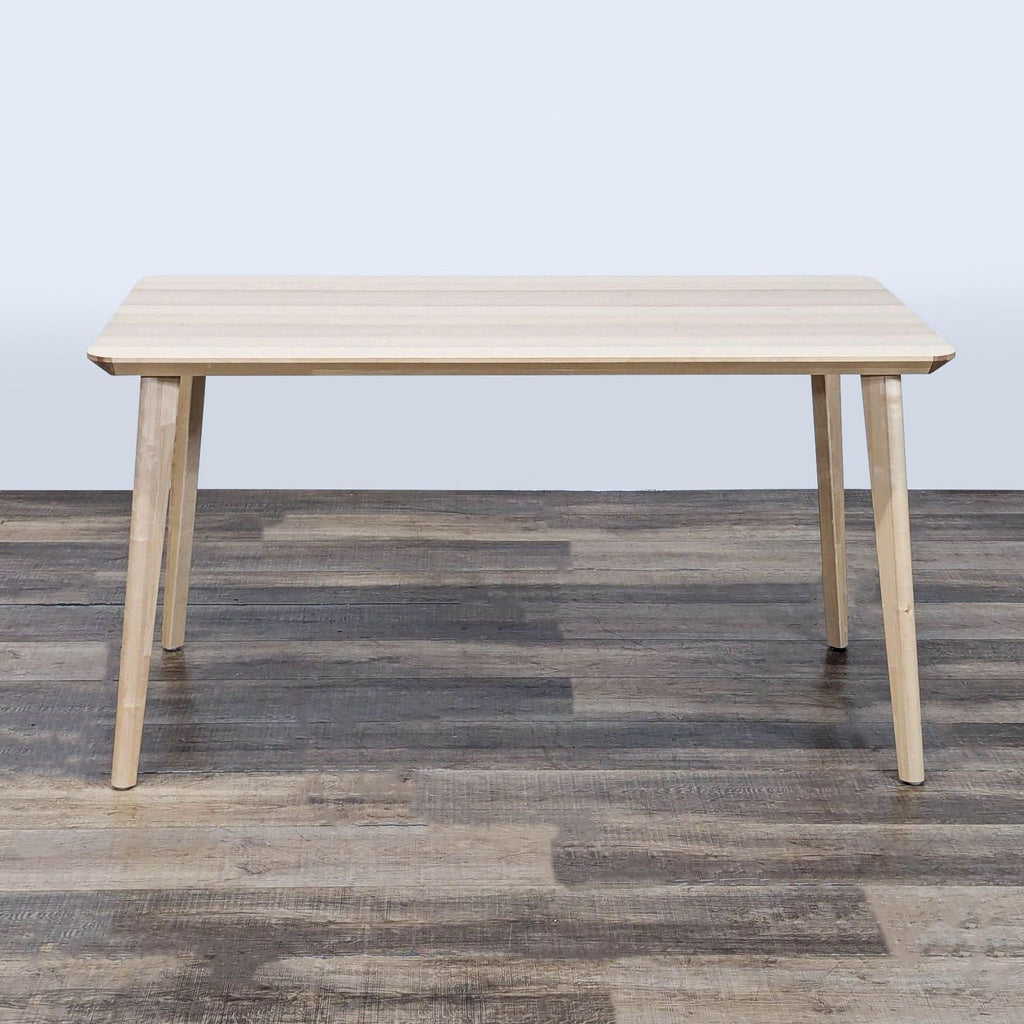 Rectangular Ikea dining table with ash veneer finish, simple design and four tapered legs, on wooden floor.  