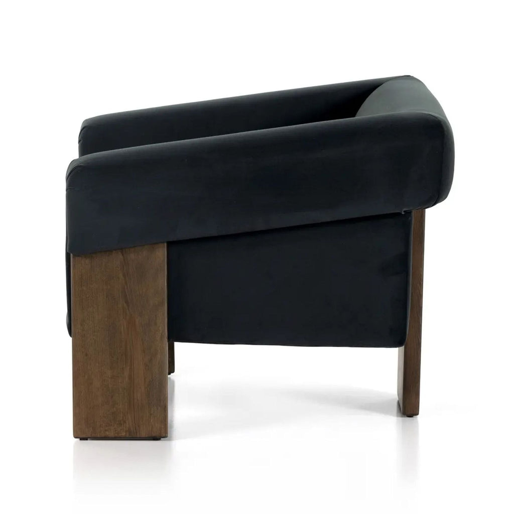 2. Side view of a Havenly lounge chair with thick wooden legs and dark velvet upholstery in a floating seat style.