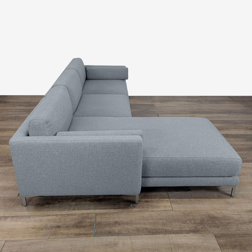 3. Side view of a CB2 sectional with chaise, track arms, and sleek metal legs on a wood floor.