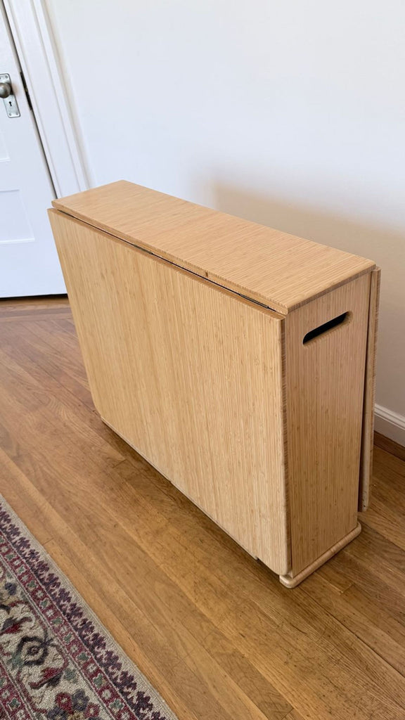 Compact Greenington dining table folded for storage, showcasing its minimalist bamboo design and handle slots.