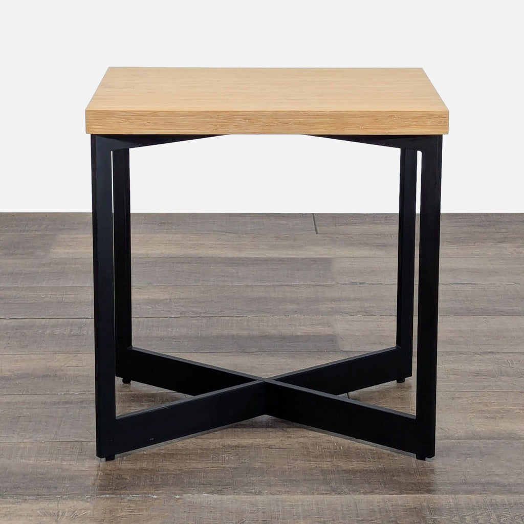 1. Reperch end table with a light wood top and black metal X-frame base on a wood floor.