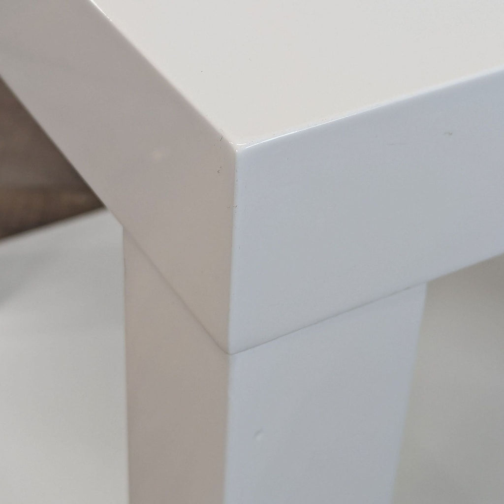 2. Close-up of the corner detailing on a glossy white West Elm side table.  