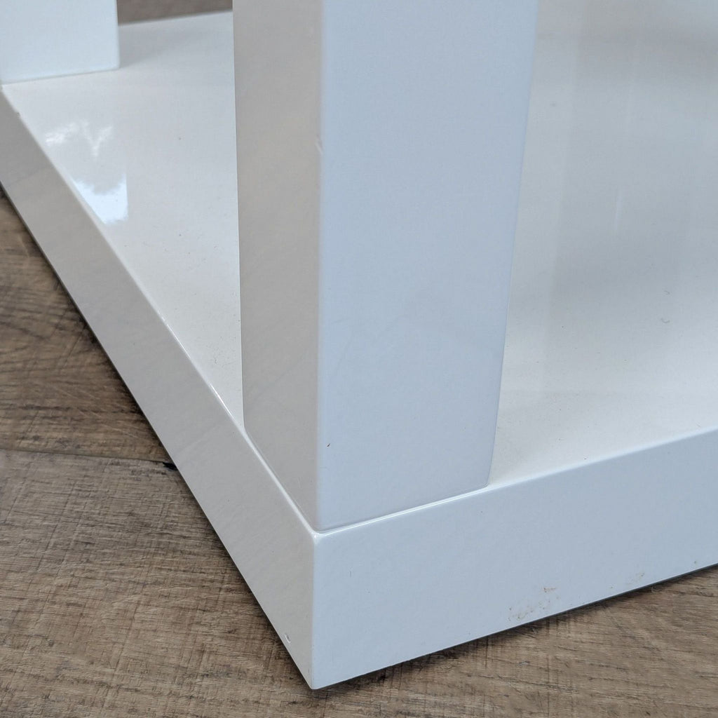3. Base corner of a glossy white West Elm side table on a wood floor, highlighting the construction.