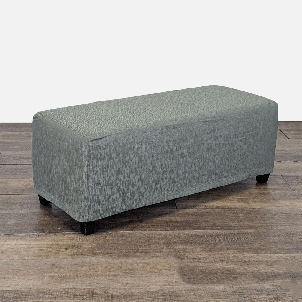 Angled view of a Reperch bench-style ottoman in textured green fabric, with short black legs on a wood floor.