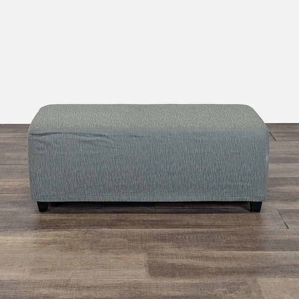 Rectangular Reperch ottoman with muted green fabric cover, shown on a wooden floor, viewed from the front.