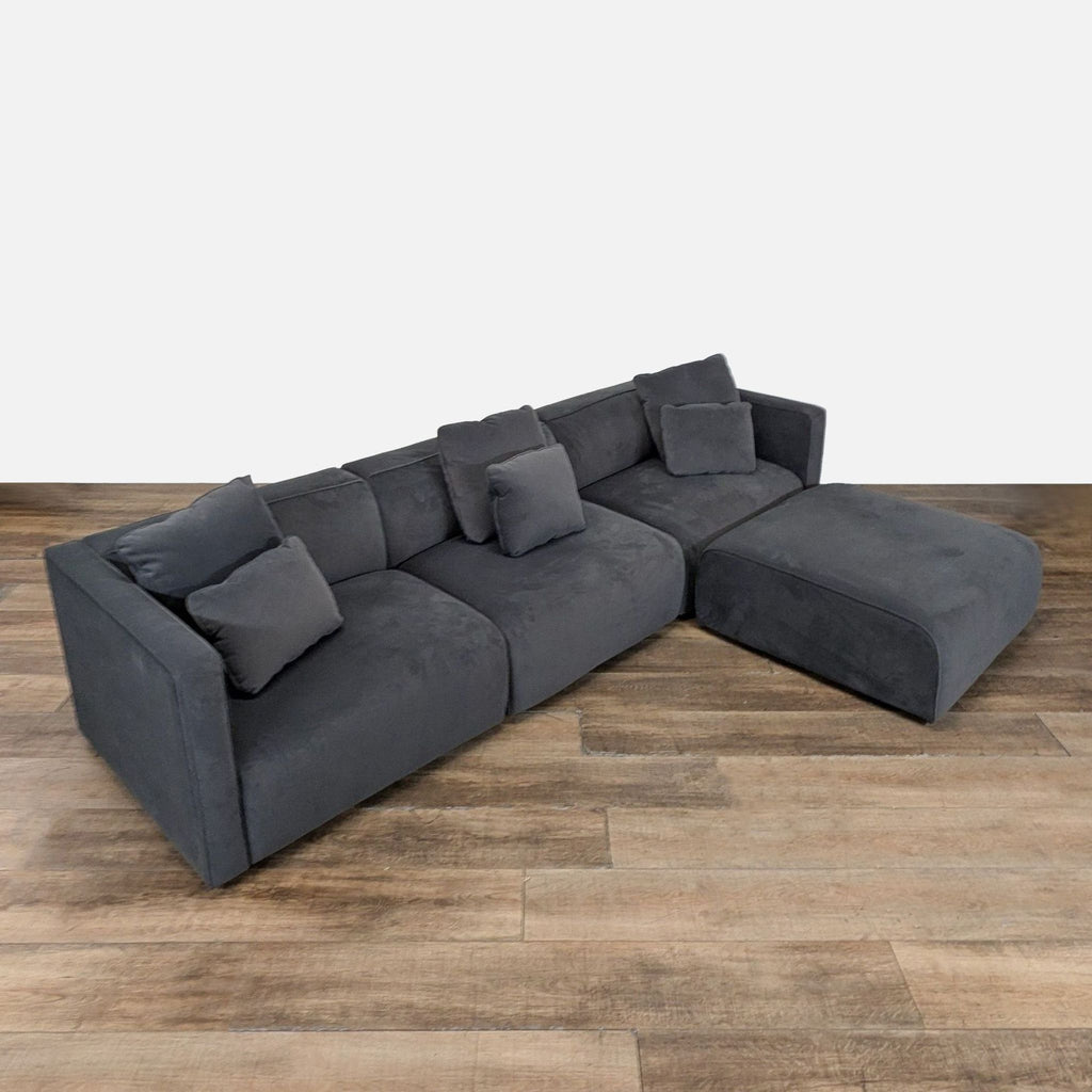 2. Angled view of a Living Spaces sectional, upholstered in dark gray velvet with matching removable cushions.