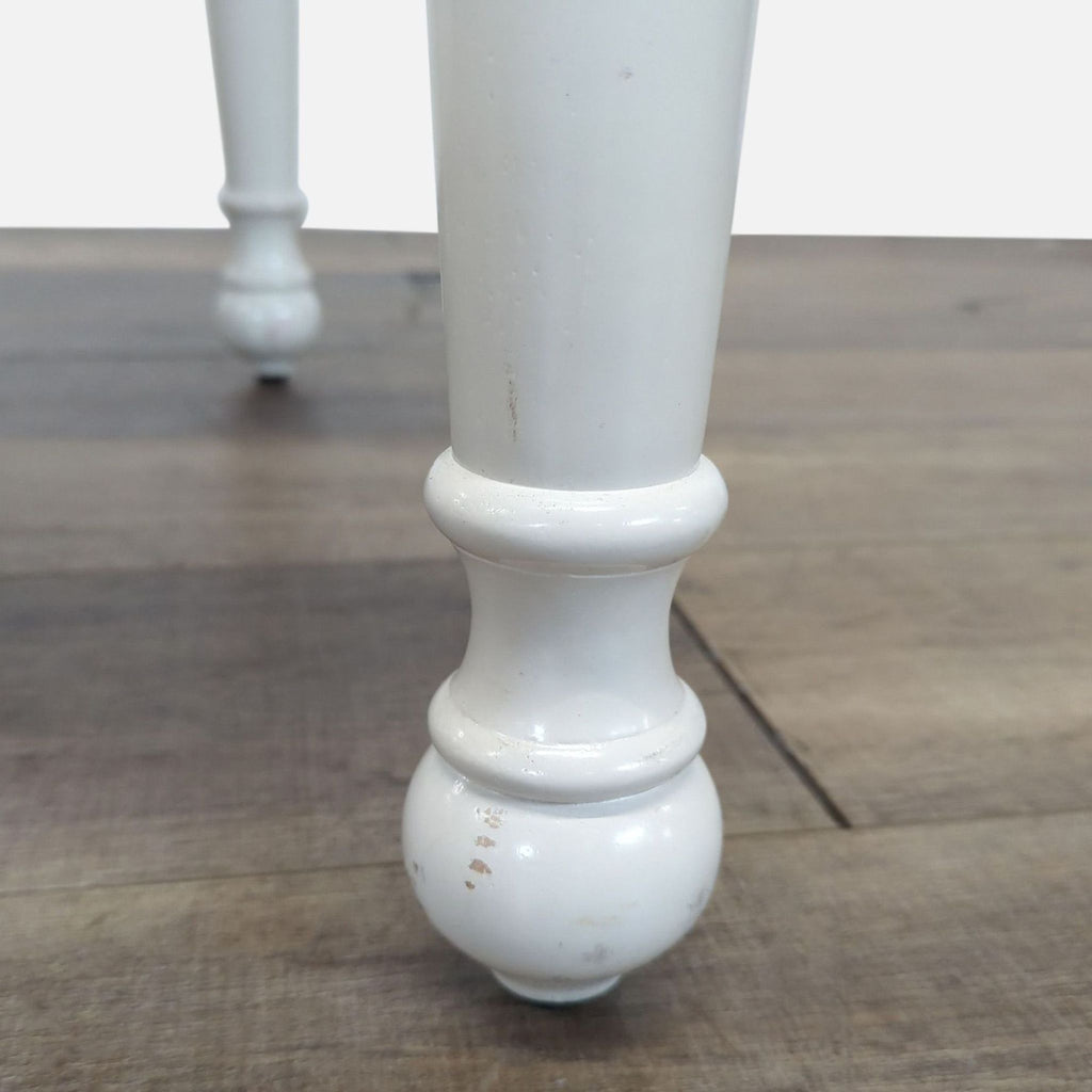 Close-up of a Reperch end table’s white turned leg, showing wood texture and minor scuff marks.