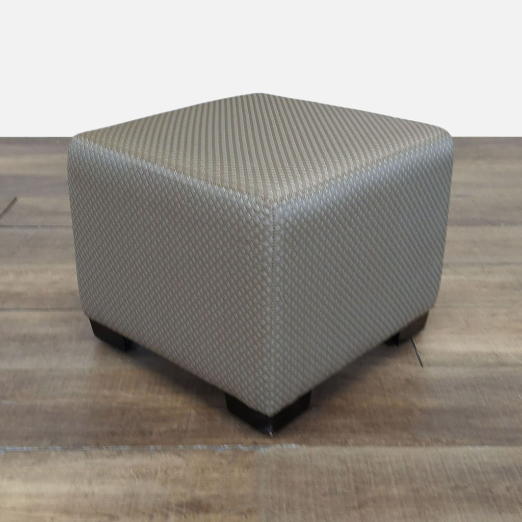 Square taupe ottoman from Cisco Bros., featuring textured fabric and wooden legs, displayed on a wooden floor.