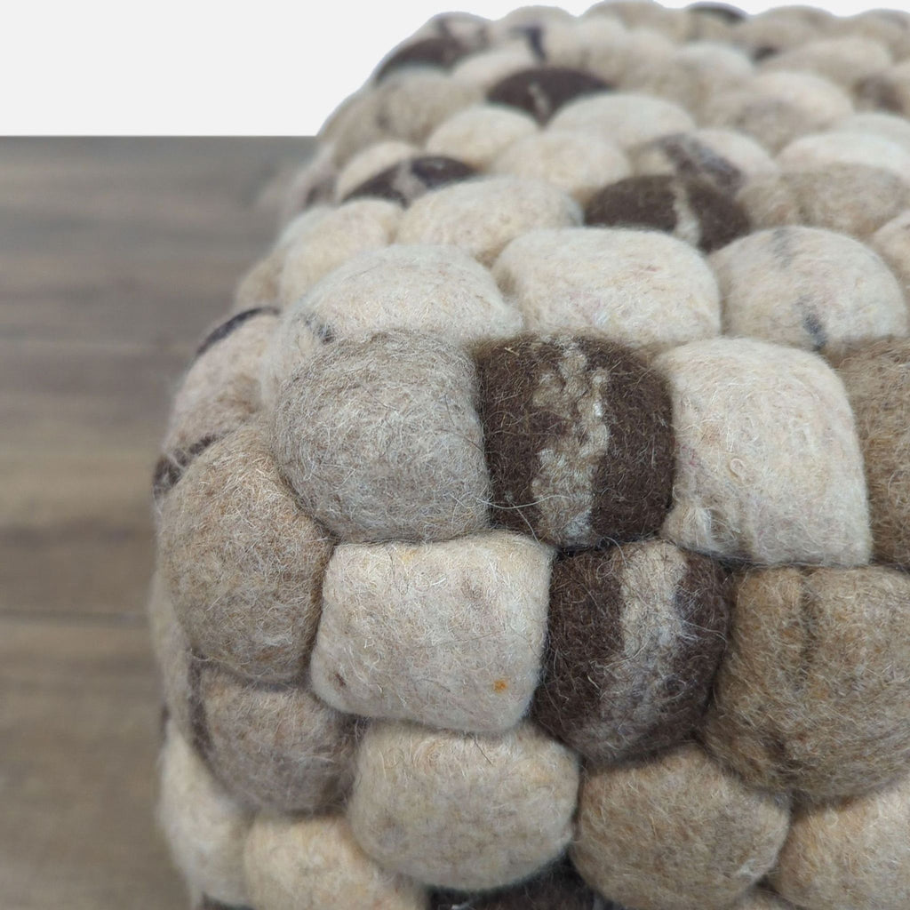 Detailed view of fuzzy woolen ball texture and color mix on Reperch’s taupe, charcoal, and gray pouf ottoman.