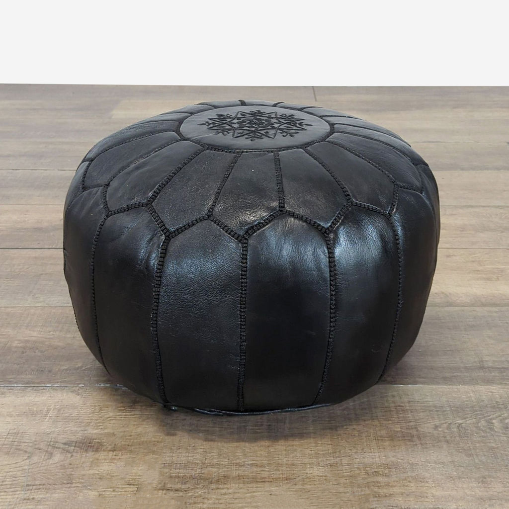 Round black leather ottoman with decorative stitching and a floral pattern on top, by Reperch.
