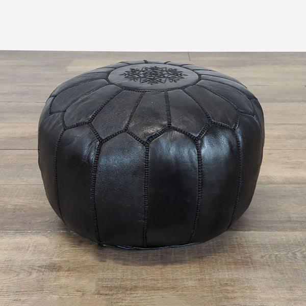 Round black leather ottoman with decorative stitching and a floral pattern on top, by Reperch.