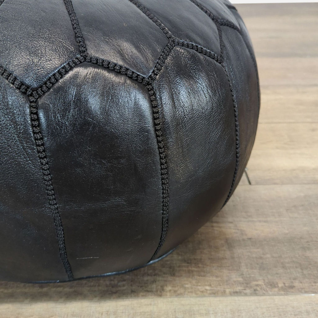 Close-up of black leather pouf’s textured stitched panels, highlighting craftsmanship and material detail.