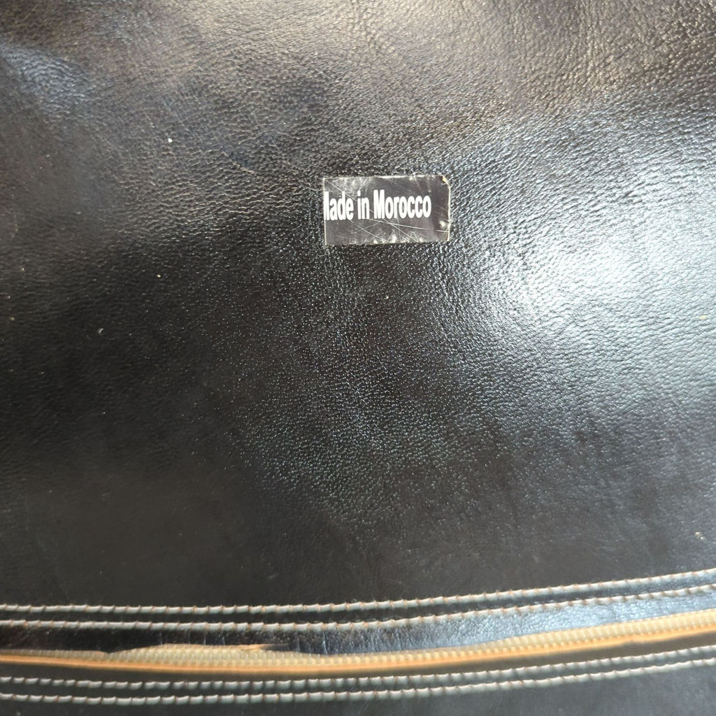 Label reading "Made in Morocco" on the underside of a black leather ottoman, next to a zipper.