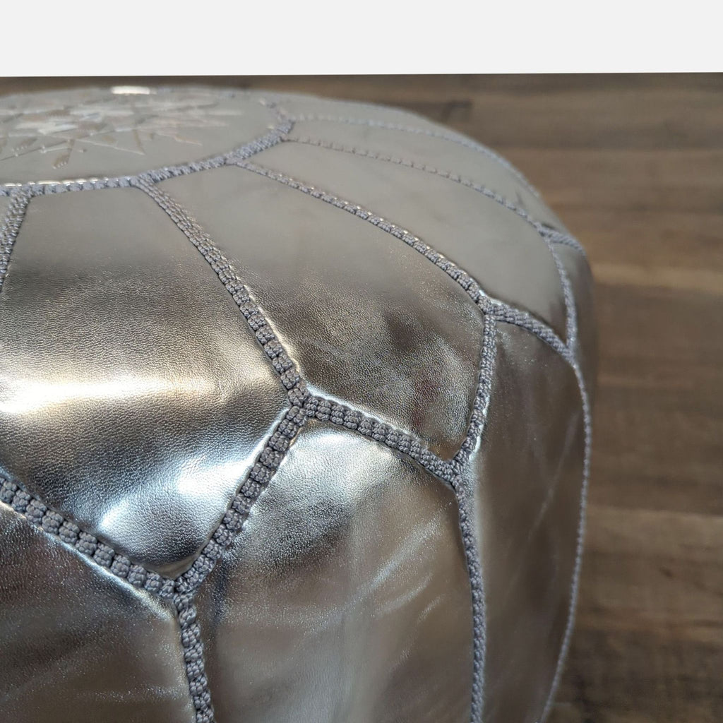 2. Close-up of Mistana silver pouf ottoman, highlighting shiny material and intricate stitched panels.