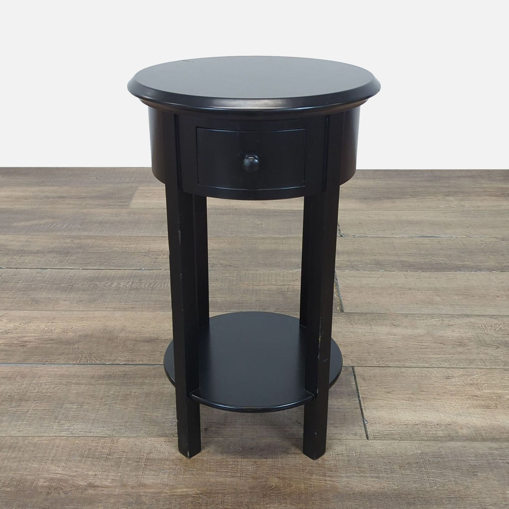Black round side table from Target with a drawer and bottom shelf, displayed on wood floor.